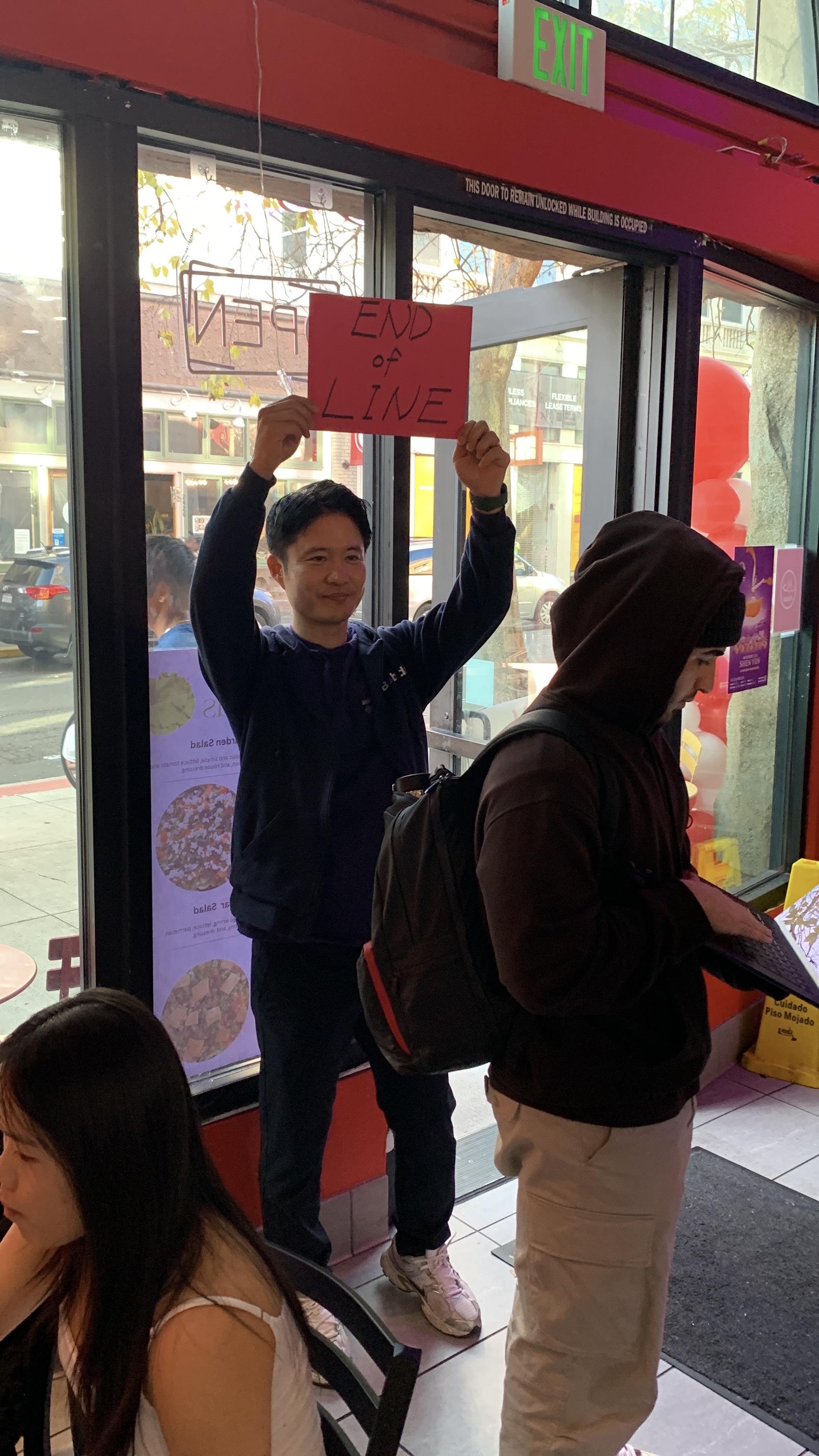 Upswell teammate holds an 'End of Line' sign at the back of a queue inside a packed partner restaurant